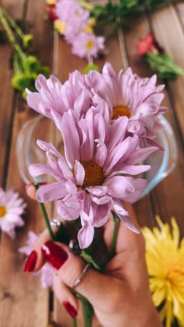 woman's hand holding a bouquet of purple daisies on a wooden table