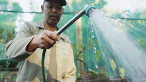 African-american-male-gardener-watering-plants-at-garden-center