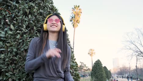 asian woman wearing wireless headphones enjoying listening to music and dancing outdoors in the city street.