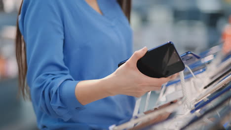 close-up of a woman in an electronics store holding in her hands two new smartphone and chooses the best one standing near the showcase with gadgets