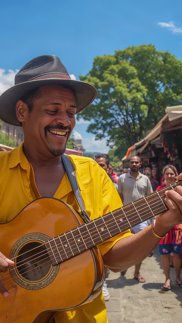 Video verticale: artista di strada sorridente con top giallo e cappello a tesa larga che suona la chitarra e canta per la folla al mercato