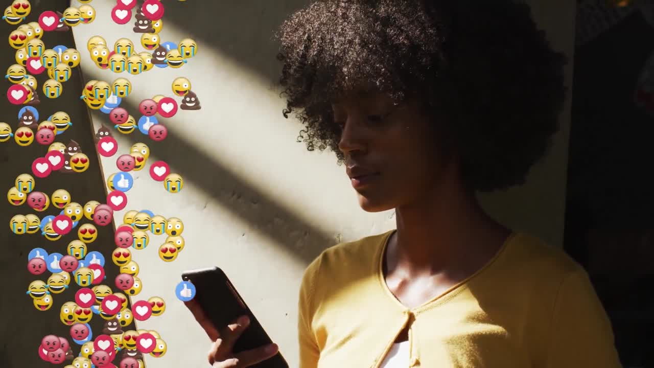 Composite video of multiple face emojis floating against african american woman using smartphone