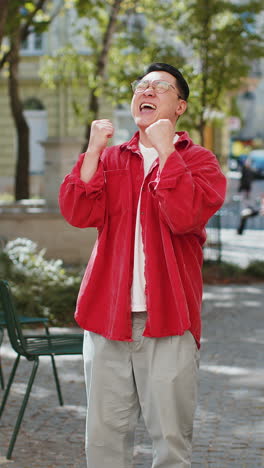 asian man shouting celebrating success winning goal achievement good victory news on city street