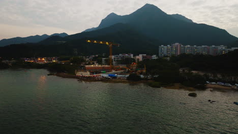 Beautiful-drone-shot-approaching-a-crane-in-a-construction-site-overlooking-a-lake