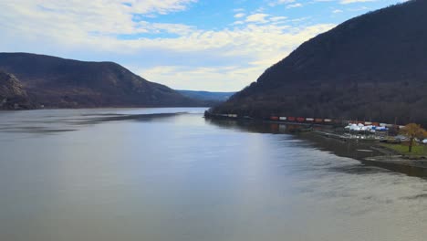 Train-at-the-base-of-a-mountain-with-a-wide-river-valley-and-mountains-on-a-sunny-day-in-late-fall