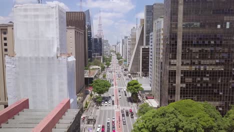 the business center of sao paulo, brazil with cars, skyscrapers, and financial buildings in street avenida paulista on a sunny day- aerial flying footage