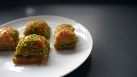 a plate with four pieces of baklava, each topped with finely crushed pistachios