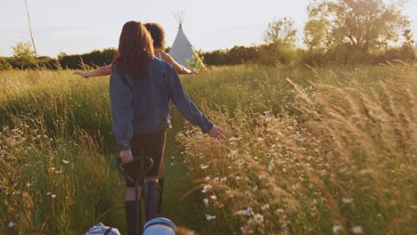 two female friends walking pulling trolley through field towards teepee on summer camping vacation