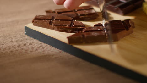 close up of person cutting bars of milk and plain chocolate into smaller pieces with knife