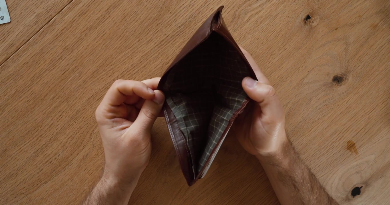 Vista superior de manos sosteniendo una cartera vacía sobre una mesa de madera. Concepto financiero de falta de dinero, pobreza, gastos, deuda y presupuesto personal.