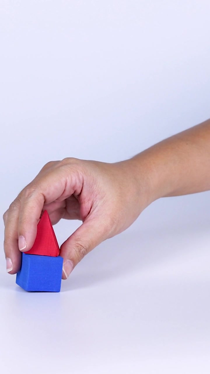 La mano de una persona organiza y equilibra cuidadosamente una pirámide roja sobre un cubo azul.