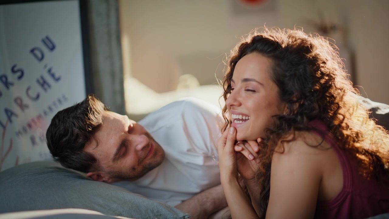 Casal apaixonado relaxando na cama sob a luz do sol da manhã. Homem e mulher felizes rindo no quarto.