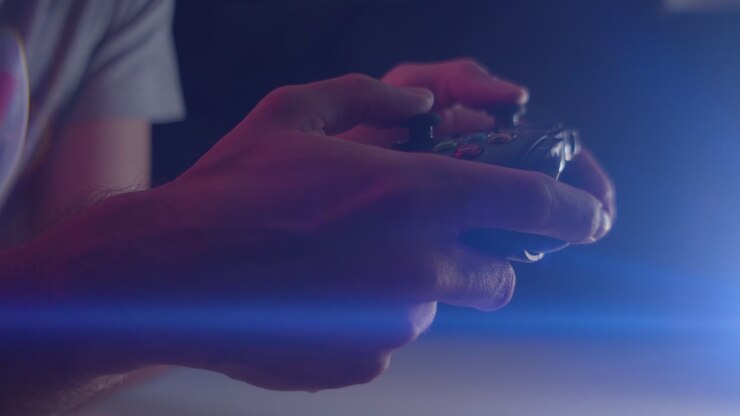 Gioco ai videogiochi in una stanza buia con un flare anamorfico dell'obiettivo sui pulsanti di un controller, riprodotto lentamente