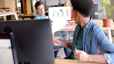 Happy-diverse-male-colleagues-passing-document-and-talking-in-casual-office,-slow-motion