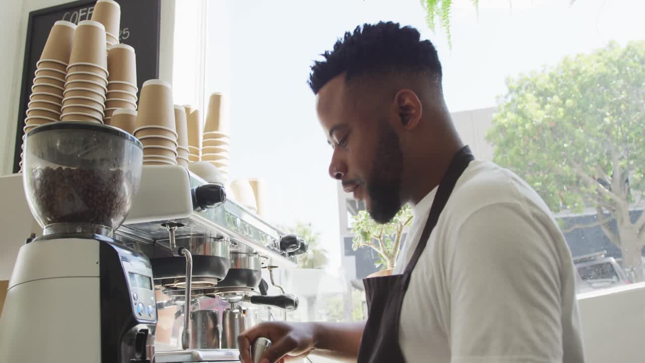 Barista afroamericano felice che prepara caffè usando una macchina da caffè in un bar.