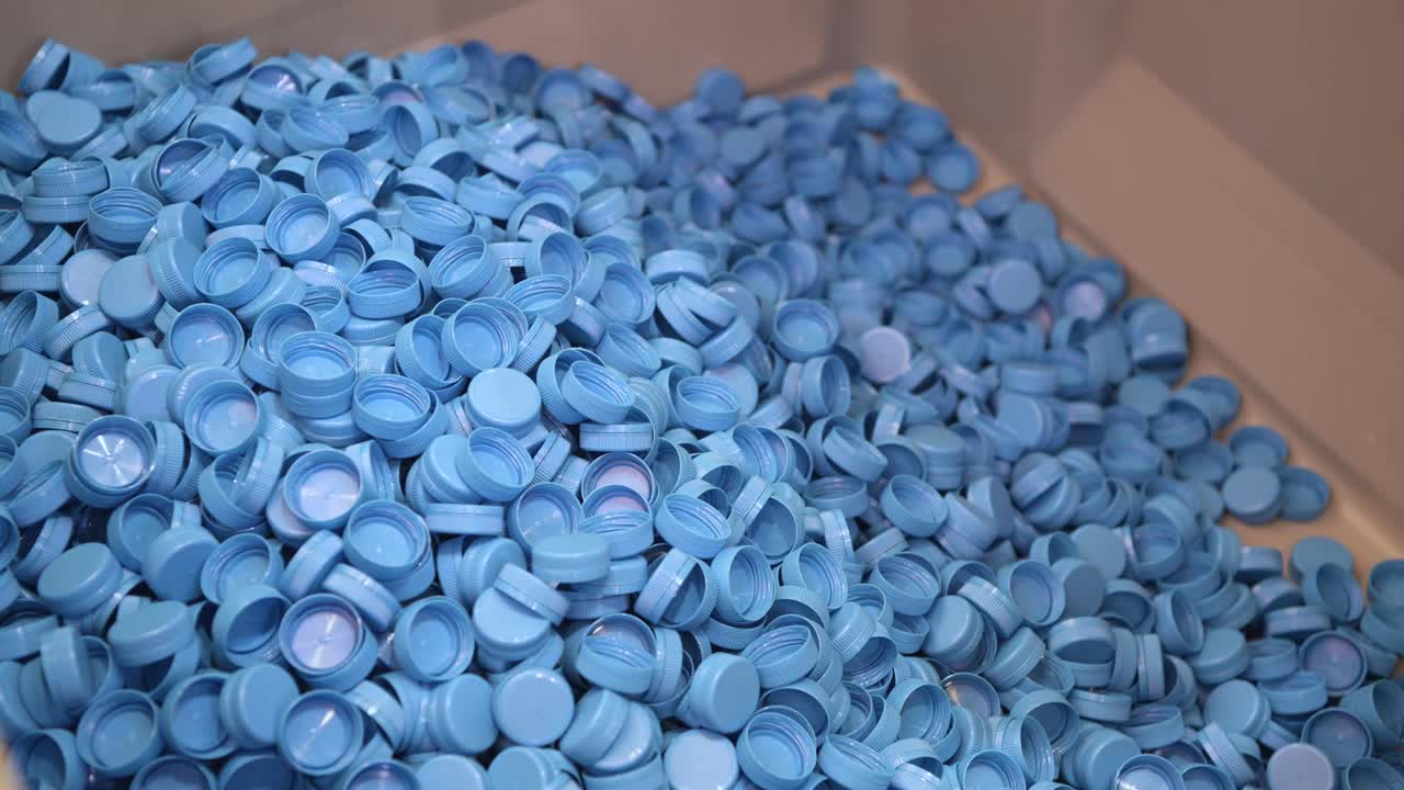 A bunch of plastic bottle caps. Blue caps fall from top to bottom
