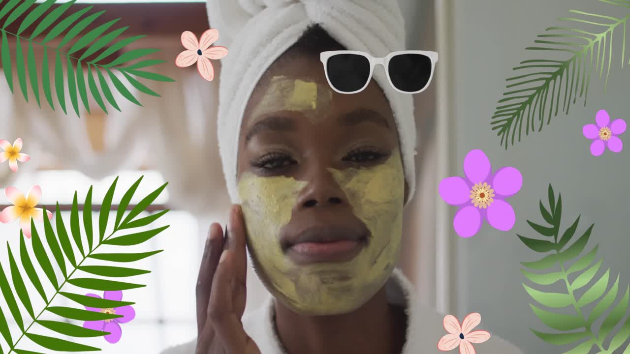 animación de flores sobre una feliz mujer afroamericana aplicando una máscara facial