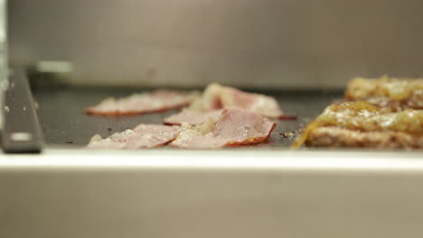 cocinar tocino y hamburguesas en una plancha de acero inoxidable, agregar una rebanada de queso encima de una hamburguesa - cerrar