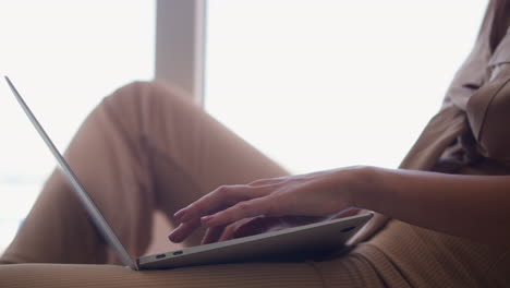 frau auf der tastatur eines modernen laptops in der nähe eines fensters zu hause