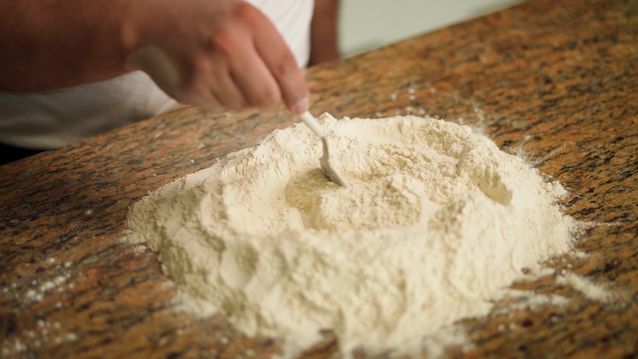 Un primo piano delle mani di un cuoco che mescolano farina secca su un bancone, preparandola per la creazione dell'impasto.