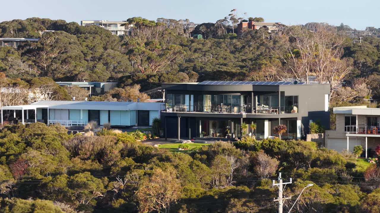 Aerial lateral tracking shot of contemporary home surrounded by dense Australian bushland in daylight