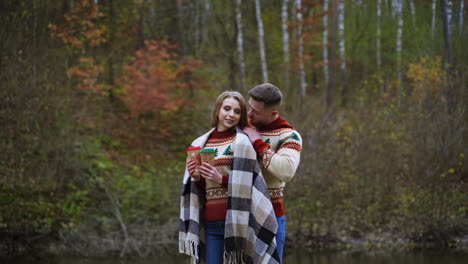 romantic couple on autumn forest background. handsome guy together with his girlfriend having a date outdoors. young girl holds two glasses of coffee.