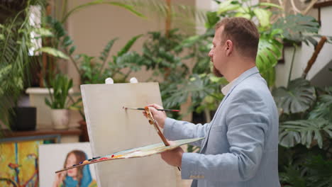 artist makes color strokes on empty canvas. inspired man in casual jacket draws picture with wide brush in studio. talented painter creates artwork