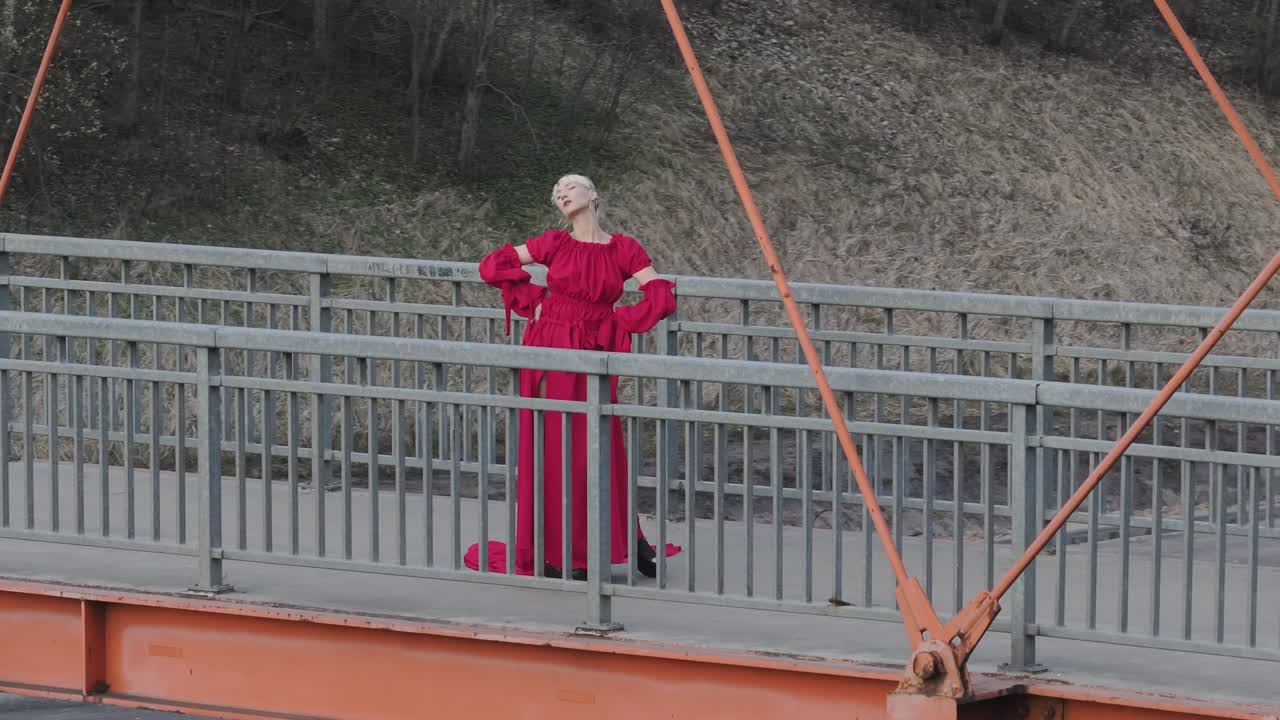 A dramatic shot of a model in a red dress posing on a bridge