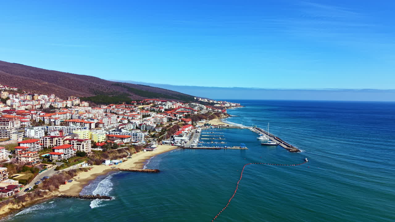 Vista costiera di una vivace città di mare con edifici, barche e acqua cristallina in una giornata di sole.