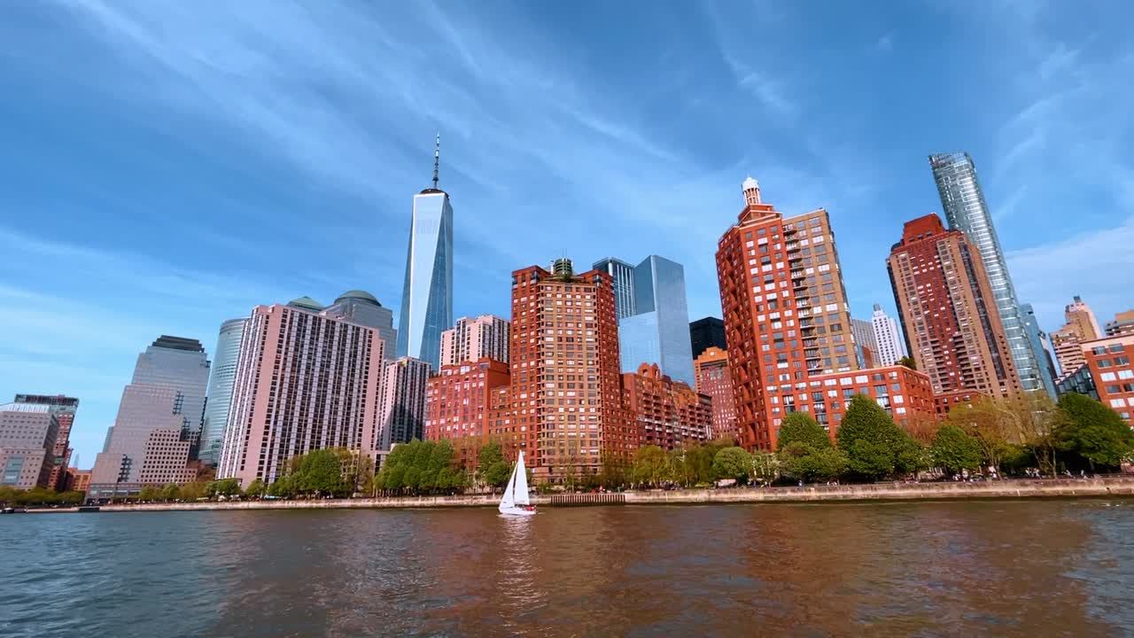 Edifici residenziali sul lungomare a Lower Manhattan con barca a vela. Torri di appartamenti in mattoni e One World Trade Center con una piccola barca a vela bianca sul fiume.