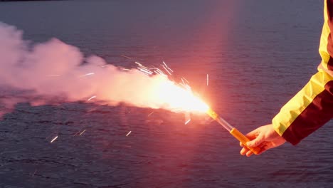 primer plano de un tripulante del barco sosteniendo una bengala de señal de emergencia, fondo de agua de mar