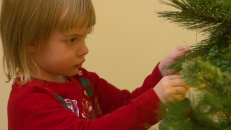 An-adorable-toddler-girl-places-a-homemade-ornament-on-a-Christmas-tree