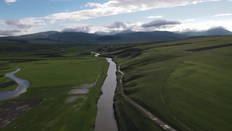 Aerial-shot-of-a-river-surrounded-by-meadows-villages-old-houses-mountains