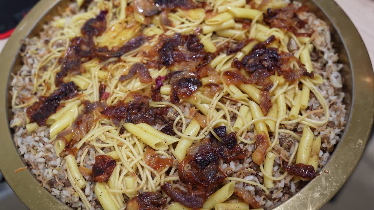 エジプトのコシャリ料理を上からクローズアップ。お盆に盛られたご飯、パスタ、レンズ豆、クリスピーに揚げた玉ねぎが食欲をそそります。中東料理、ケータリング、メニューのビジュアルにぴったりの屋内フード写真。