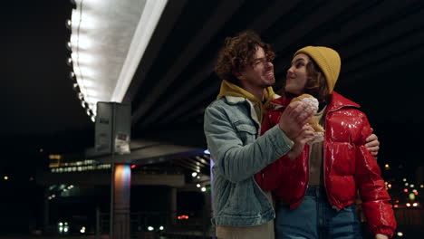 Love-couple-eating-burgers-on-city-background.-Man-and-woman-felling-happy.