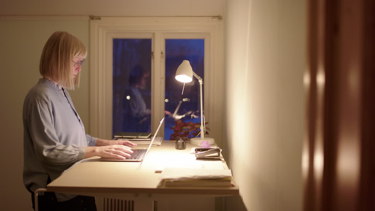 Female entrepreneur use standing desk to work online on laptop at night