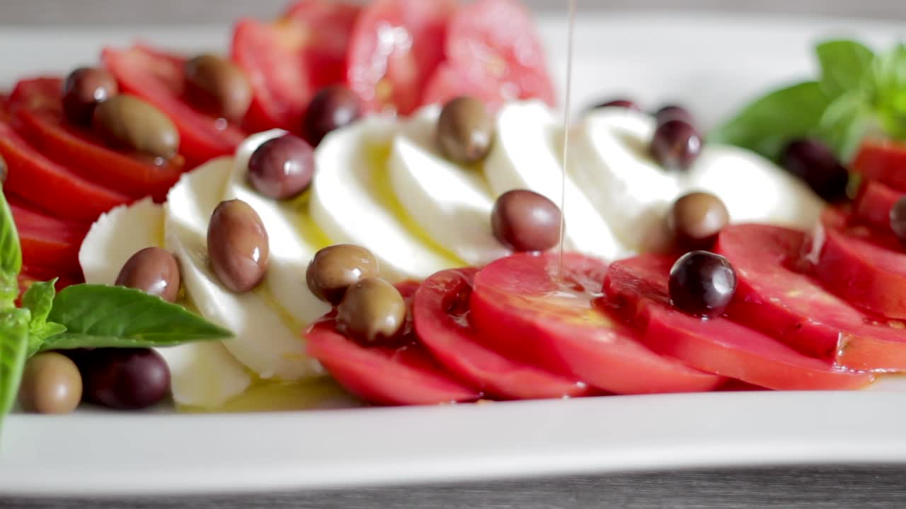 Pouring oil on Italian caprese. Typical food with tomato salad, mozzarella cheese and basil. Sliding shot. Italy healthy fresh vegetarian food. Mediterranean diet.