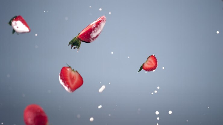 SUPER SLOW MOTION shot of fresh sliced strawberries flying with yogurt or milk drops against blue background. Shot with high speed camera, 420 FPS