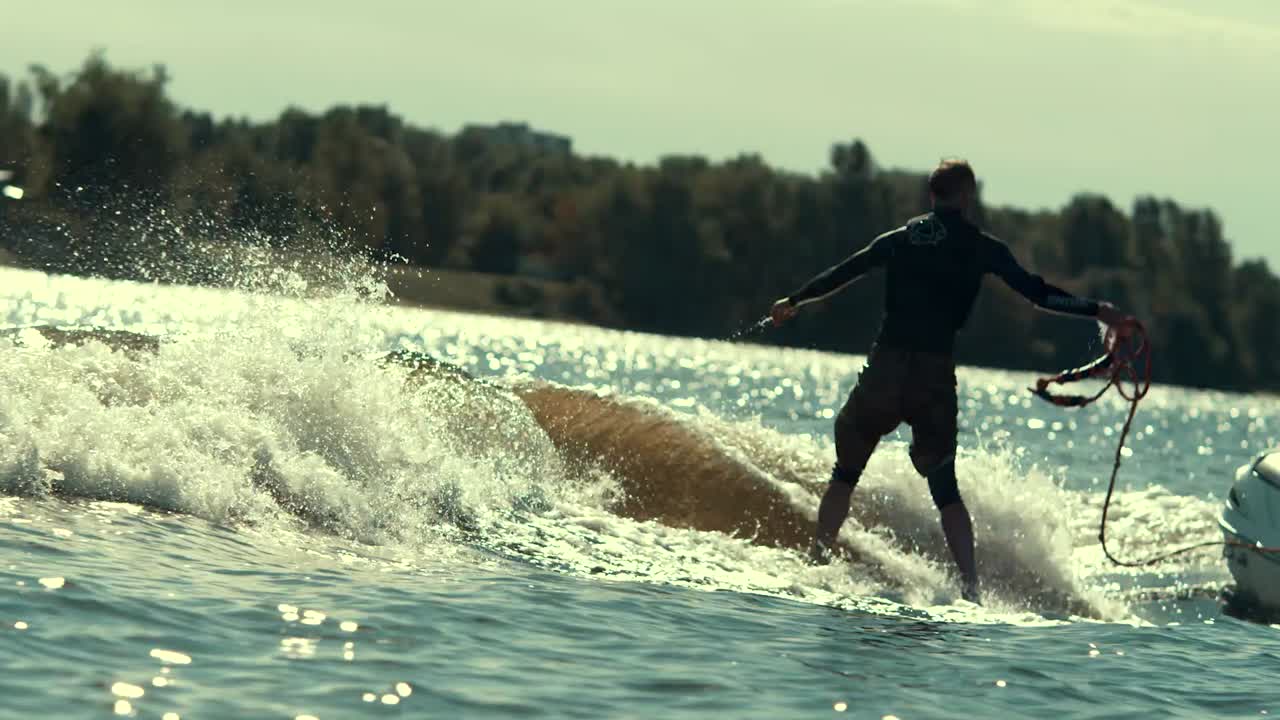deportista activo haciendo wakeboarding en las olas en el río y lanzando cuerda