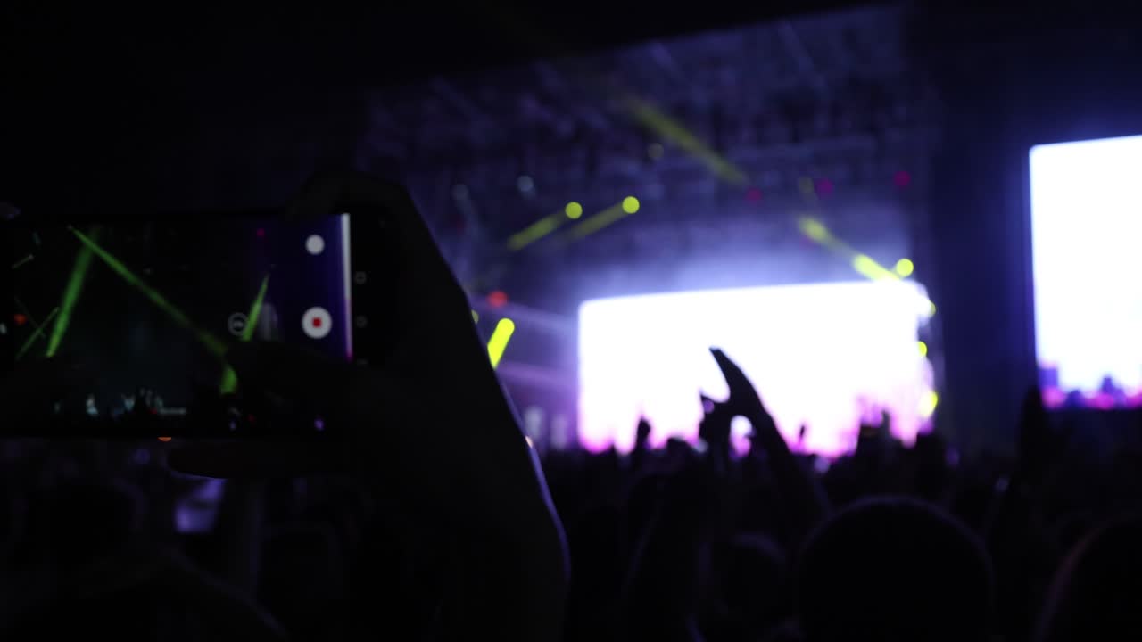 Mãos de fãs gravando vídeo com as luzes de smartphones acesas e dançando em shows de música à noite.