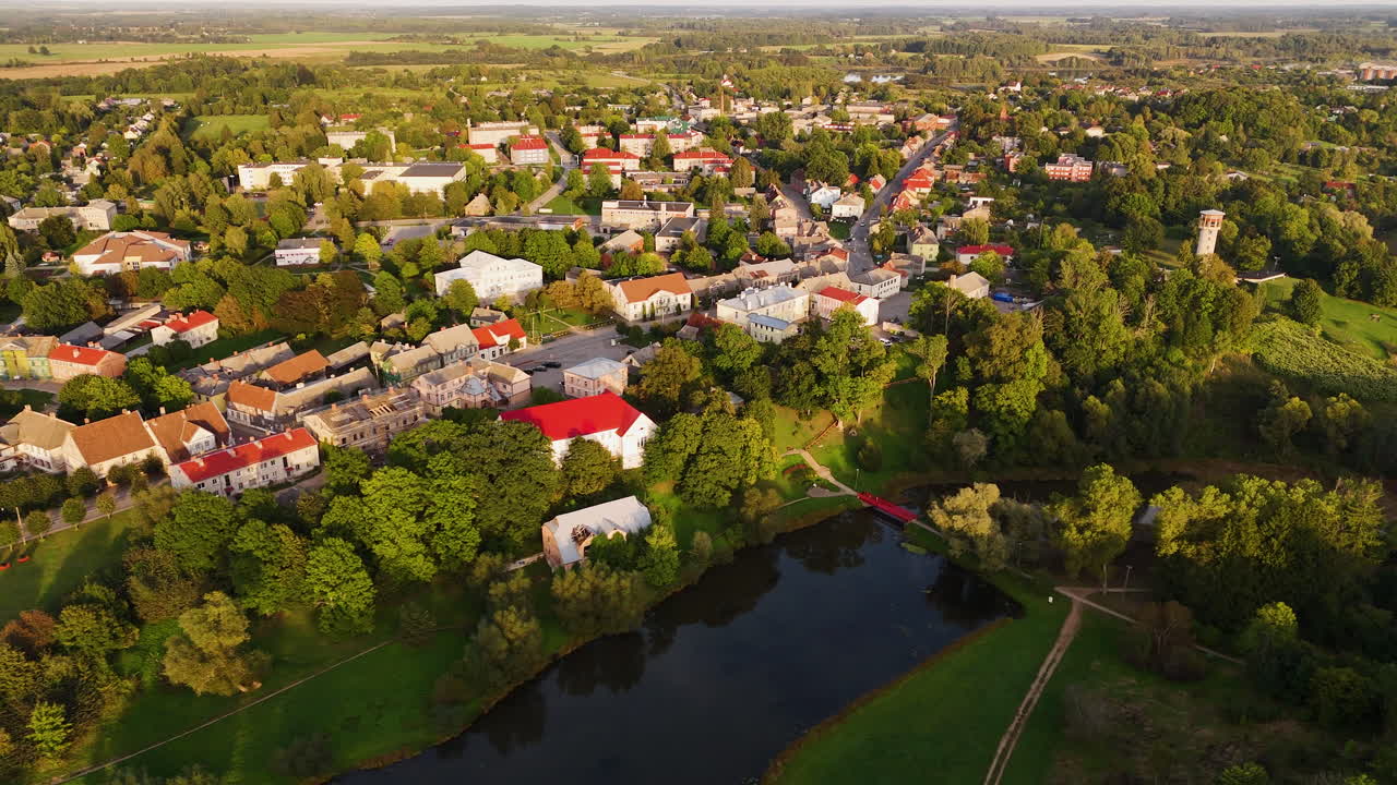 Old Historic Town Of Aizpute In Latvia, Northeastern Europe. Beautiful Aerial Views Flying Over The Tebra River.