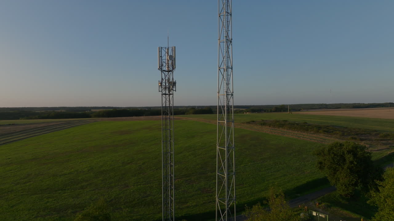 dos torres celulares en el medio de las tierras de cultivo durante el amanecer, la órbita aérea se inclina hacia arriba