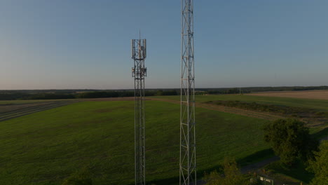 two cellular towers in the middle of farmland during sunrise, aerial orbital tilting upward