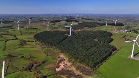 wind turbines, cornasaus, county cavan, ireland, april 2023. drone pulls backwards with a wide view of windmills spinning over green farmland during a clear warm morning.