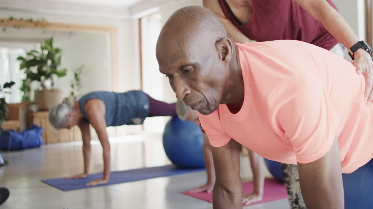 Diverse seniors using exercise balls in pilates class with female coach, unaltered, in slow motion