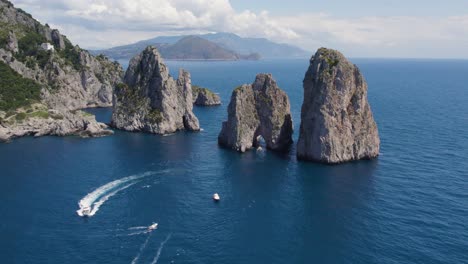 boats exploring geological phenomenon of faraglioni sea stack rock formations, aerial
