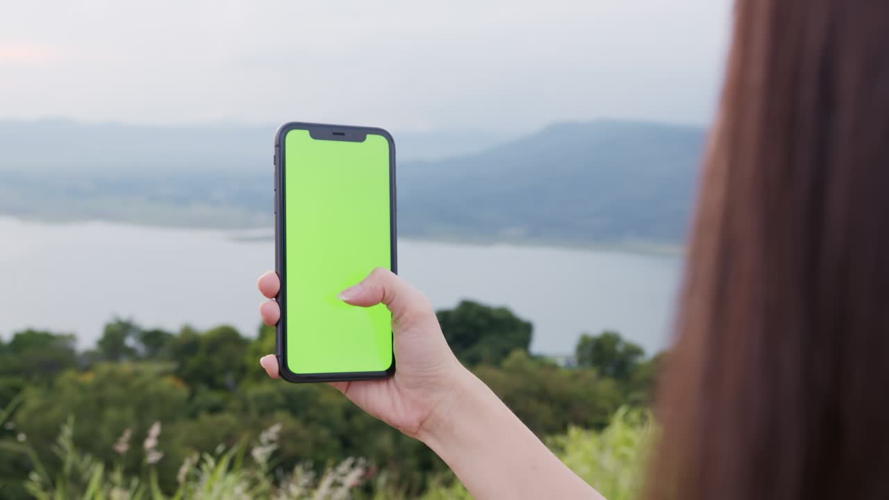 tiro de mano: mujer turista sosteniendo un teléfono de pantalla verde por la noche y una mujer usando una máscara para prevenir enfermedades.