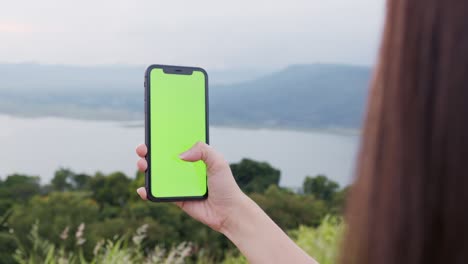 handheld shot : woman tourist holding a green screen phone at night and a woman wearing a mask to prevent disease.