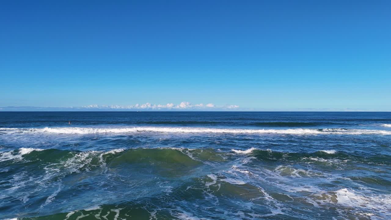 Aerial footage of ocean waves along Gold Coast, Australia. Clear skies and vibrant blue water create a serene coastal scene