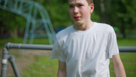 a close-up of a young boy intensely focused and preparing to block an incoming ball while standing near the goalpost, with a blur view of outdoor equipment in the background